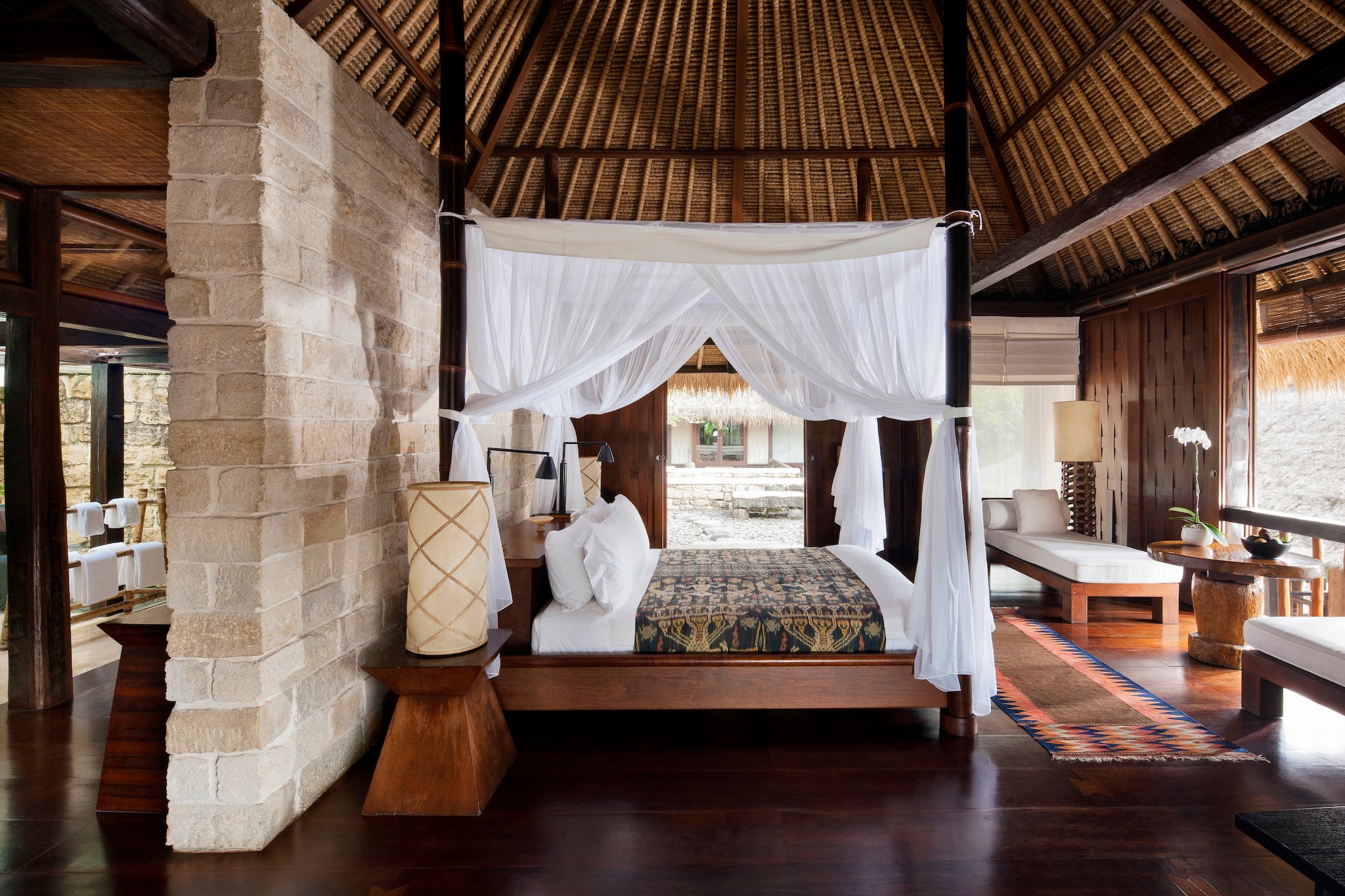 Terrace Suite Tejasuara has a brick wall dividing the bed from the rest of the room. A four-poster bed is draped with gauzy curtains.