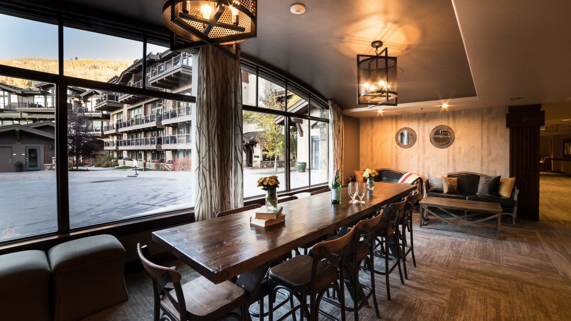 The hotel's common area has a dark wooden table and small leather couches. Gauzy curtains with a branch-like pattern frame wide windows.