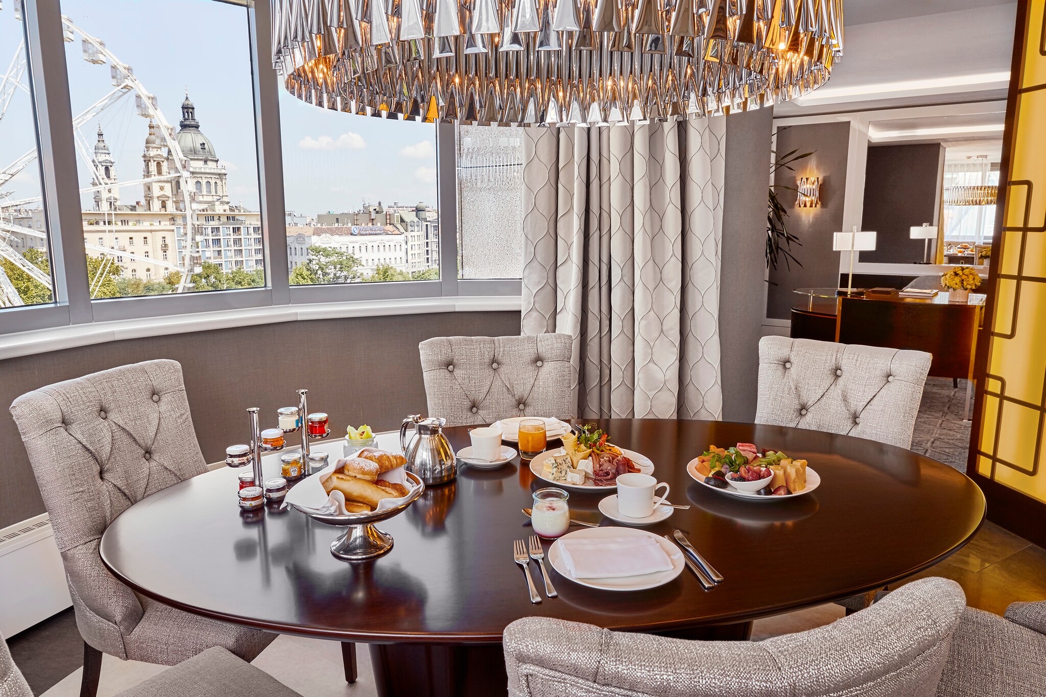 A dining table in the Corvinus Art Collection suite is set with an elegant breakfast while a ferris wheel spins out the window.