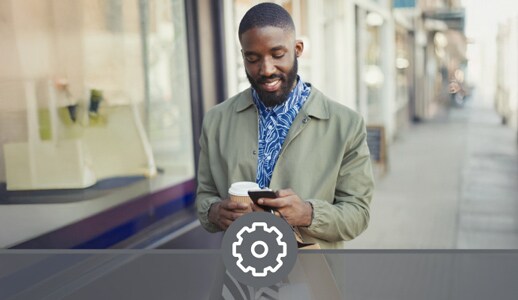 A Black man with several shopping bags and a to-go cup of coffee manages his Debit Card on his phone.