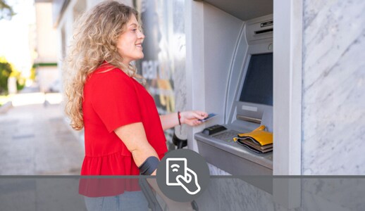 A white woman with a bright red shirt and black crutches prepares to put her Debit Card into an ATM.