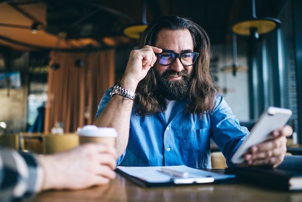 Impressed man with beard and glasses looking at cell phone