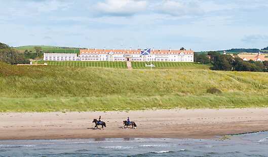Guests enjoy a beach trek on horseback along Turnberry beach, with the spectacular Trump Turnberry Resort in the background.
