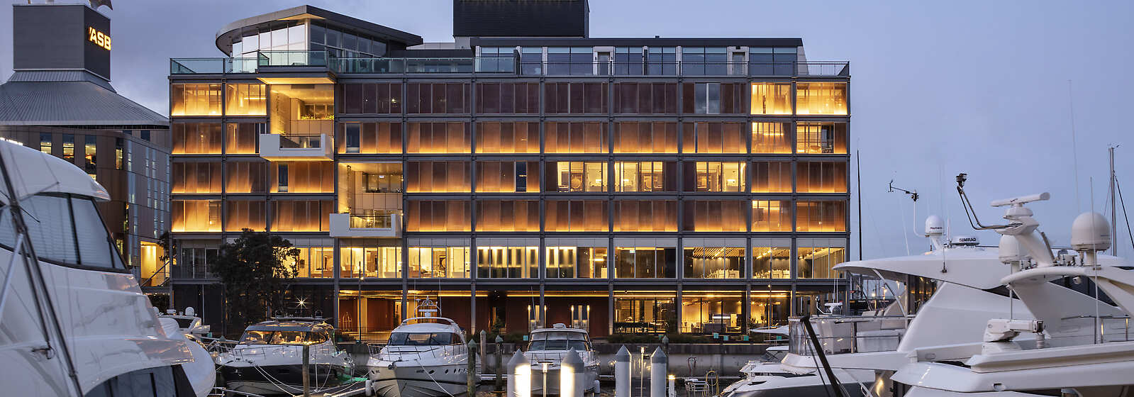 Side view of the exterior of the hotel at dusk. Surrounded by boats in the Viaduct Harbour.