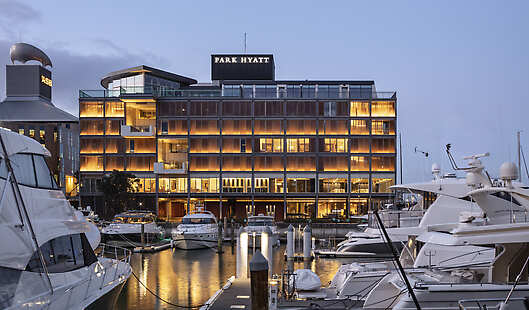 Side view of the exterior of the hotel at dusk. Surrounded by boats in the Viaduct Harbour.