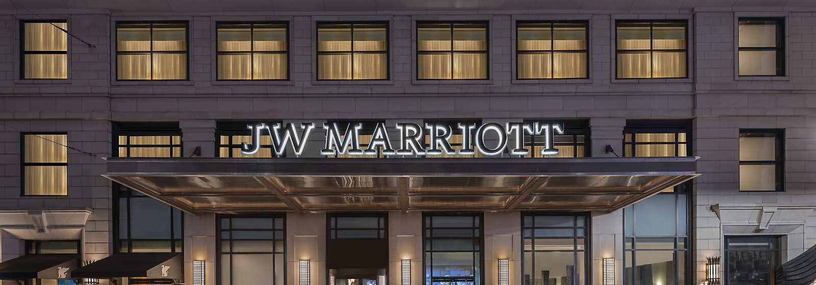 Exterior of the JW Marriott Houston Downtown at night. The building's facade is lit up, showcasing the hotel's entrance.
