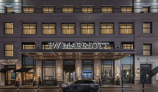 Exterior of the JW Marriott Houston Downtown at night. The building's facade is lit up, showcasing the hotel's entrance.
