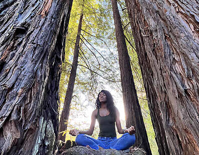 Guest in yoga pose forest bathing in redwood tree fairy ring wearing tank top.