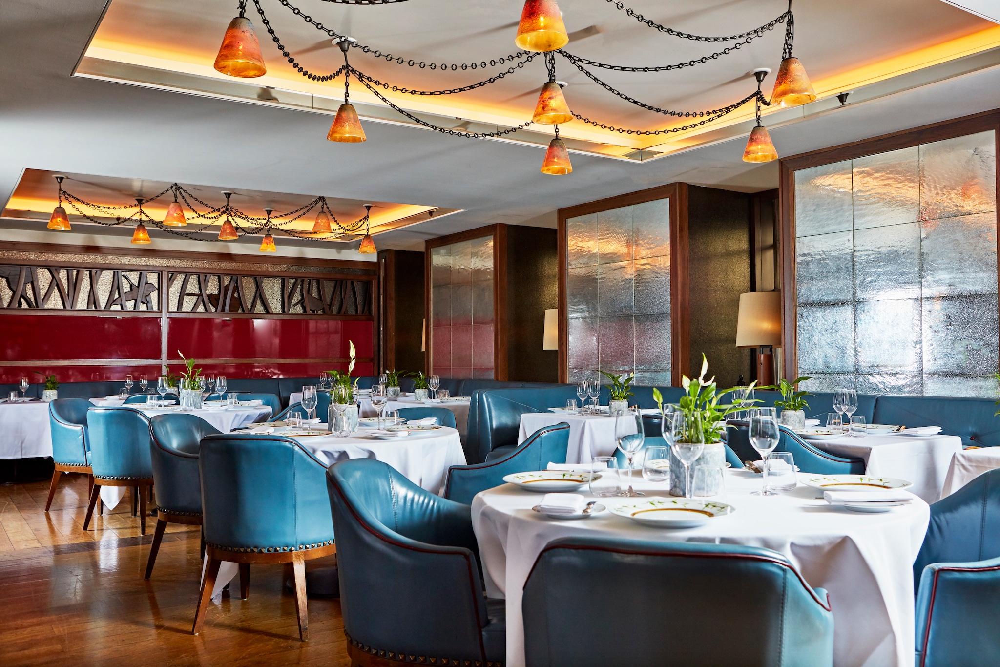 Corrigan’s dining room, with round white tables surrounded by blue leather chairs. Strings of bell-like orange lights hang from the ceiling.