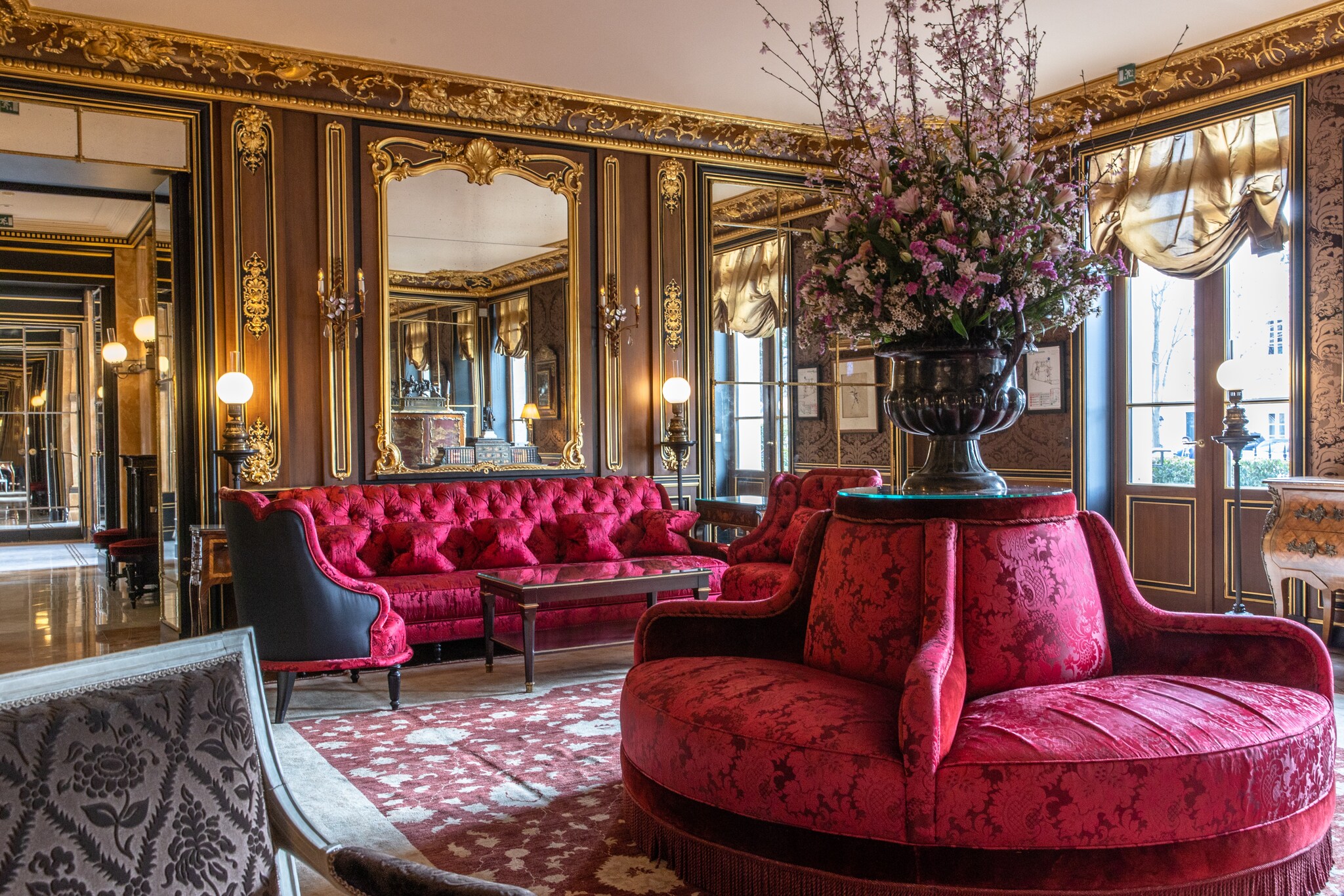 The Louis XV Salon in the hotel lobby is ornate, with wood-paneled walls with gold trim, and couches with rich red upholstery.