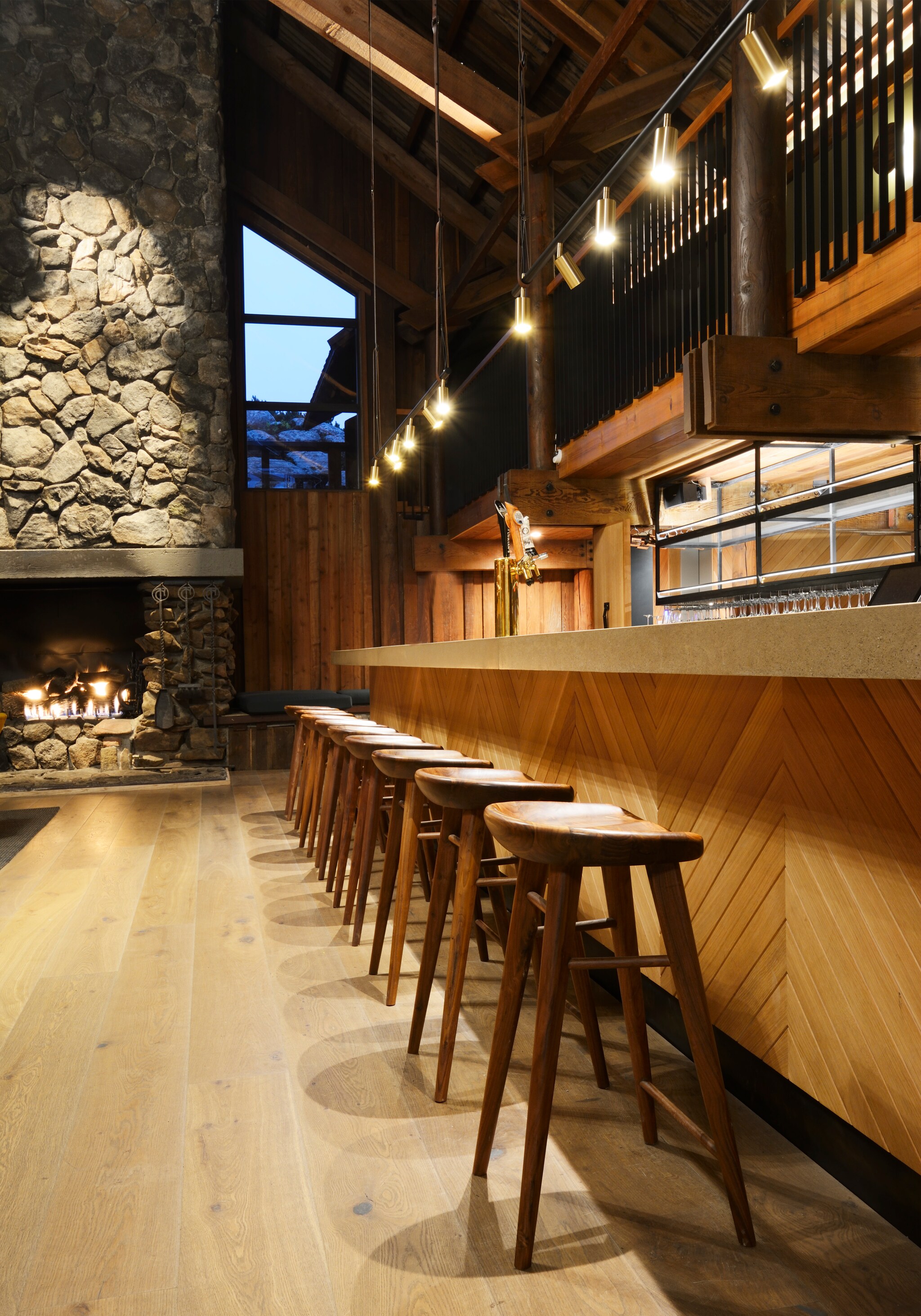 The Coast Kitchen Bar has parquet paneling next to carved wooden stools. In the background, a stone fireplace roars.