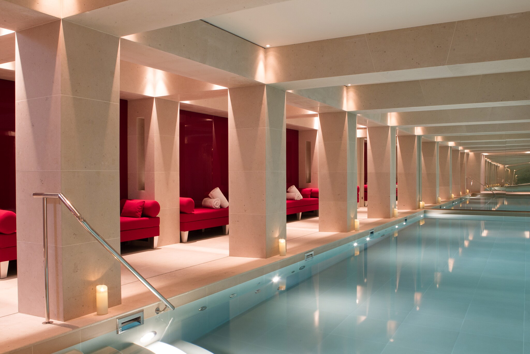 The indoor pool is capped by a mirrored wall, making the tan room with recessed red loveseats appear even bigger.
