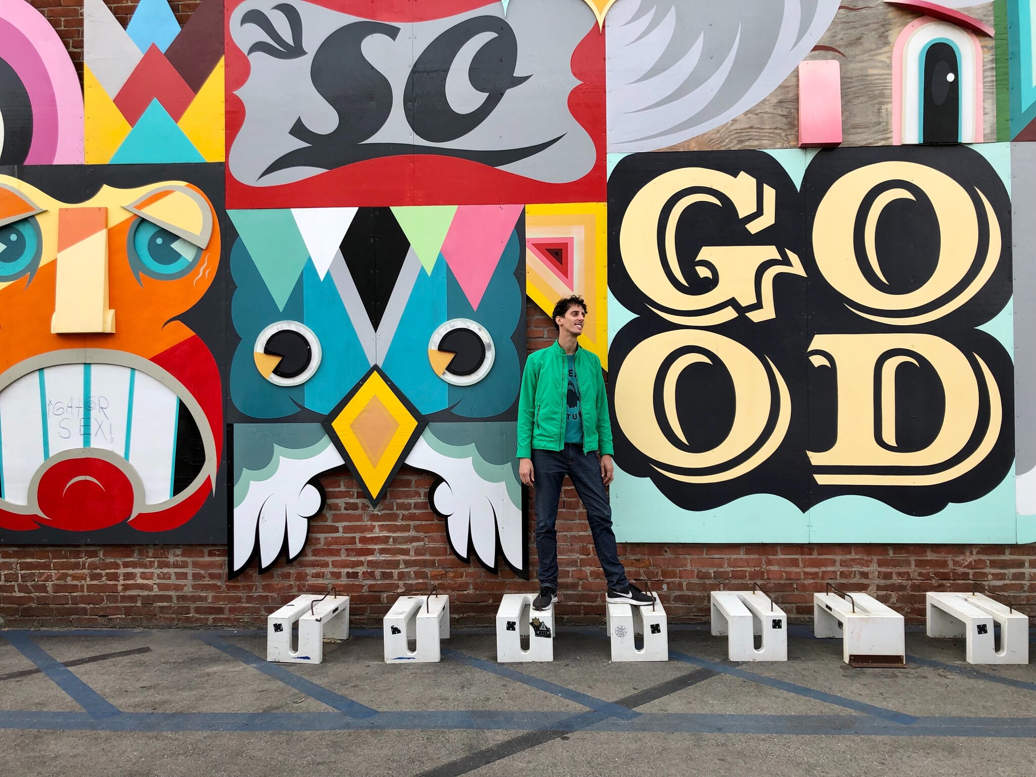 View from behind as bicyclists and walkers travel away from the viewer along the boardwalk between stretches of sand and palm trees.