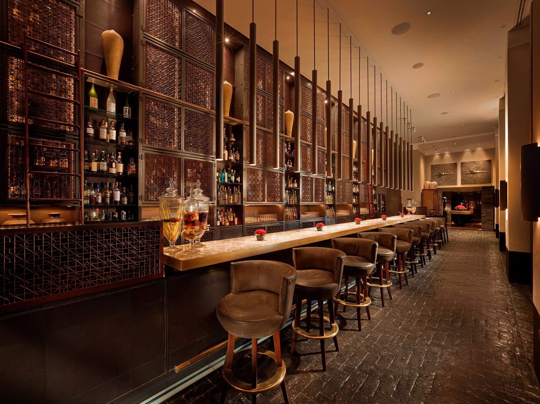 A long row of elevated chairs line the hotel bar. Delicately carved screens behind the bar barely conceal rows upon rows of spirits.