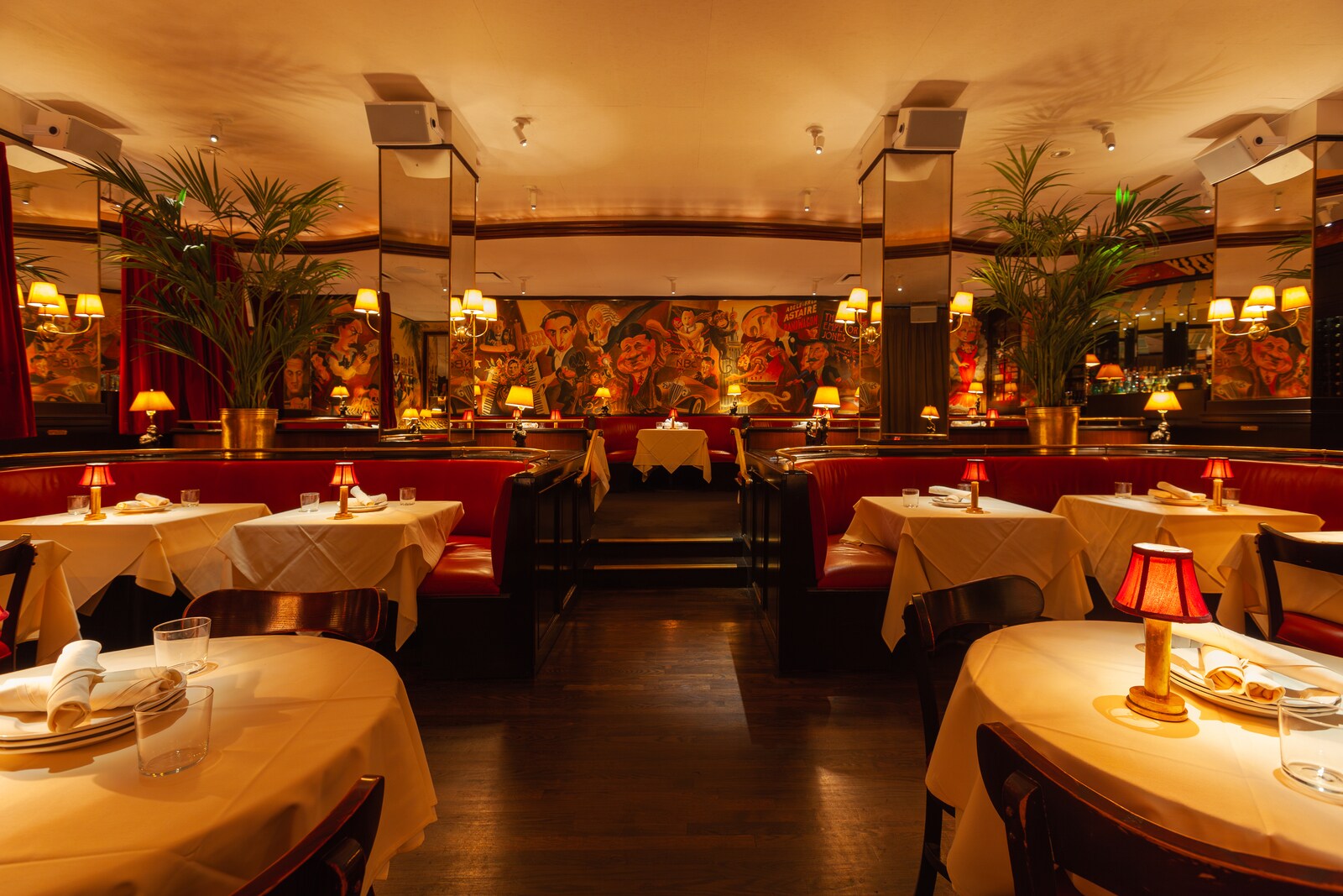 Monkey Bar is filled with red booths and mirrored pillars. Small lamps cast it in warm light and one wall is covered in cartoonish murals.