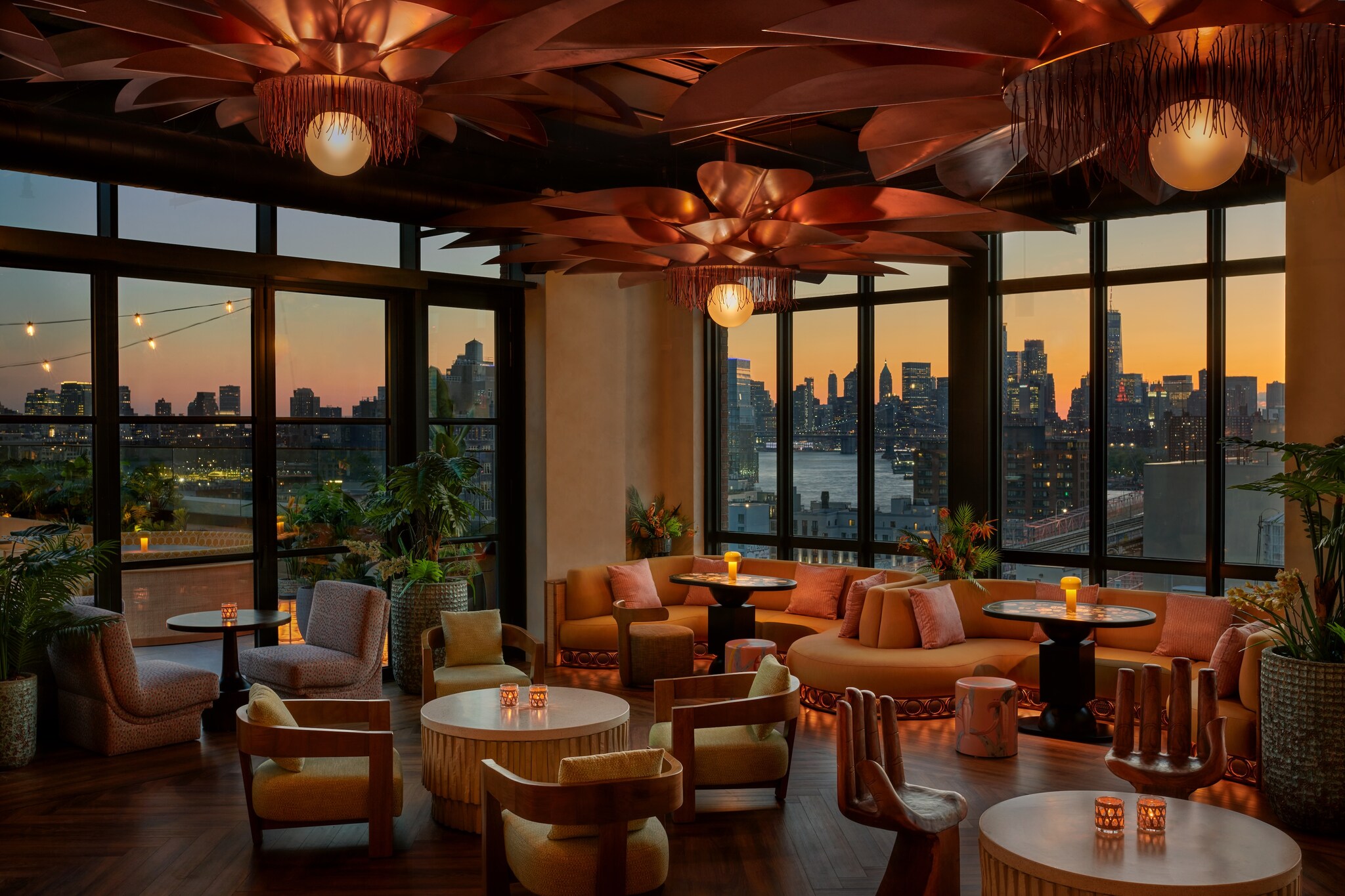 In the LilliStar rooftop bar, curved orange couches adjoin windows overlooking the city sunset. Flower-like chandeliers hang over the tables.