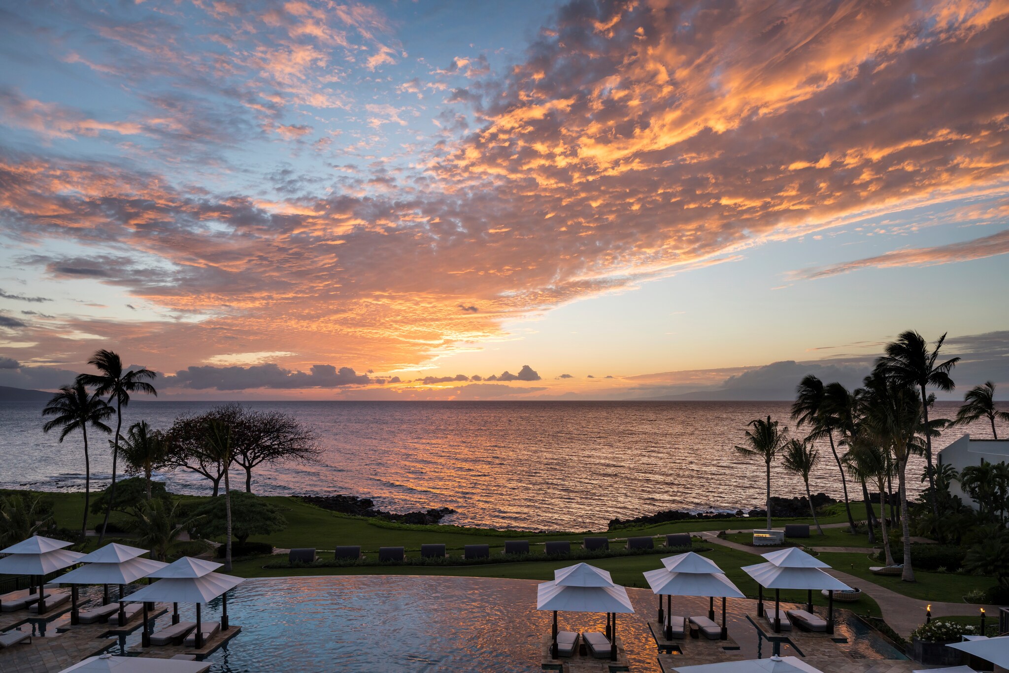 View from Wailea Beach Resort, over the cabanas, pool, and green lawn sloping down to the beach at sunset.