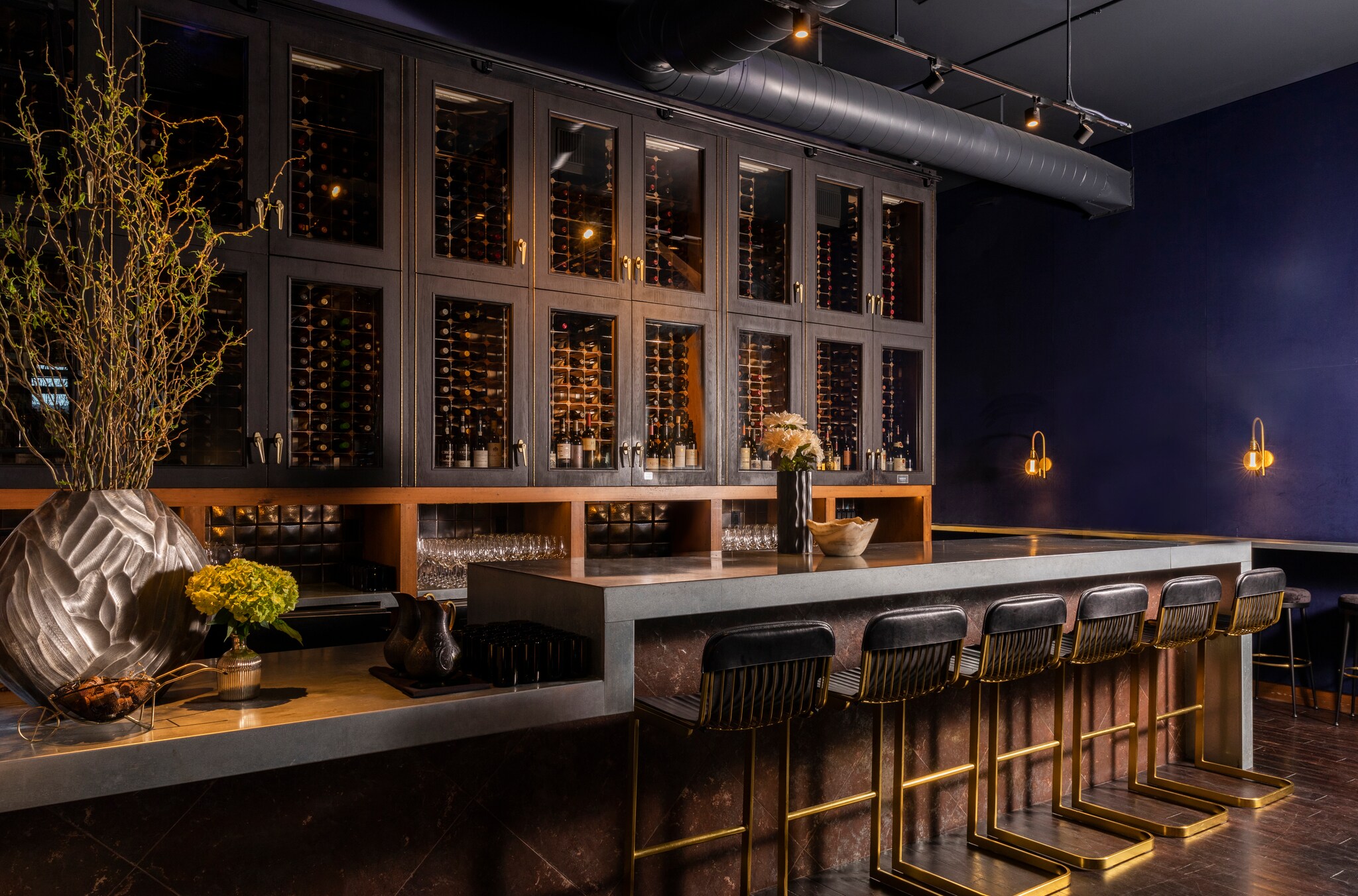 The bar at the San Francisco Wine Society is dark, with a wall of black cabinets of wine and a two-tiered black bar lined with stools.