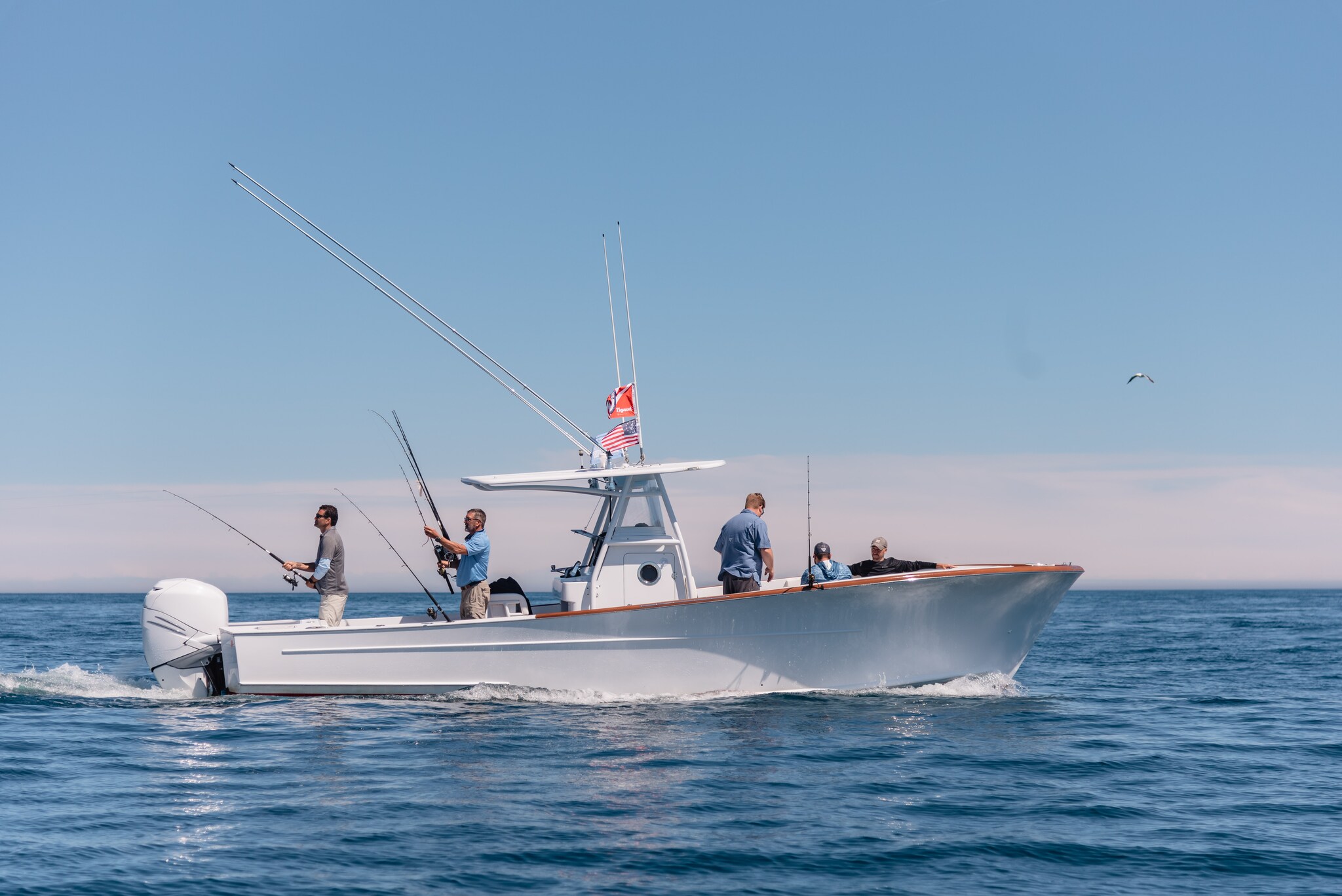 A white motorboat powers through the water while several men in blue and gray shirts fish off the sides.