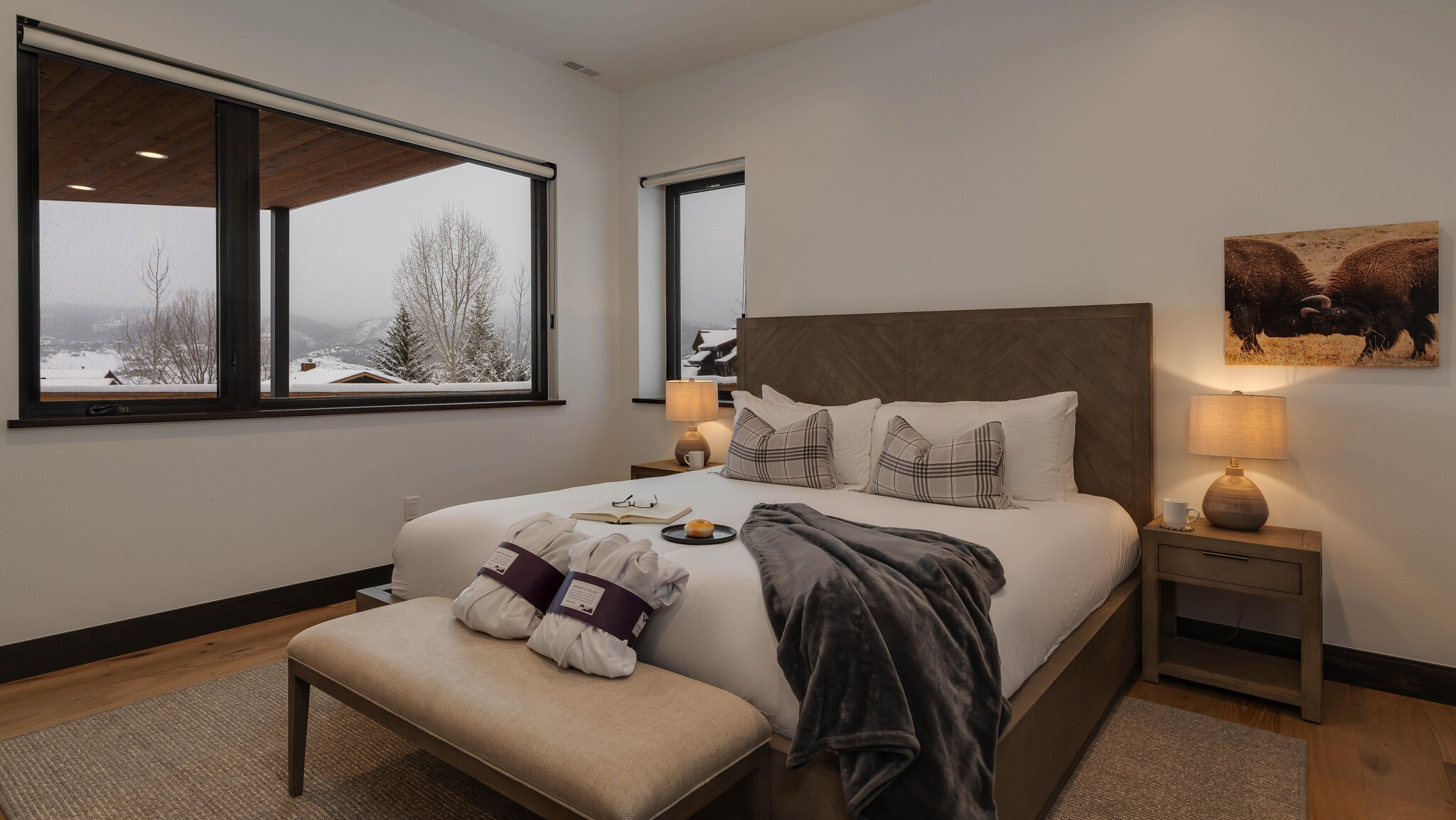 Modern bedroom interior with expansive windows showcasing mountain views in winter.