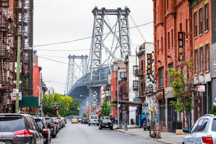 Between brightly colored buildings, power lines, and street lights, the Williamsburg Bridge stretches into the misty distance.