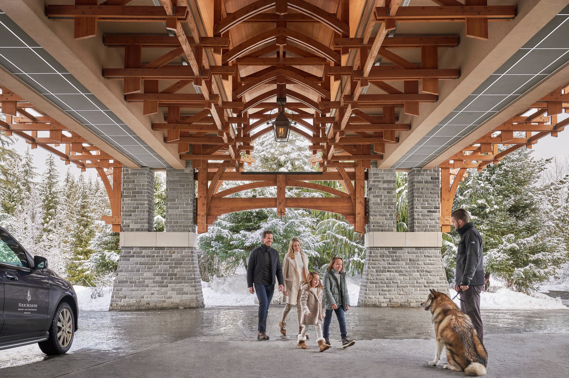 On a snowy day, a white family with two young daughters walks under the covered entrance to meet a male employee with a big fluffy dog.