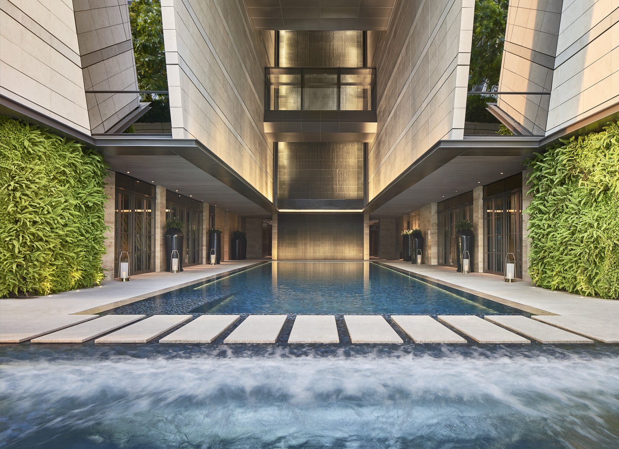 At the indoor-outdoor pool, a stone walkway separates a rectangular indoor pool from a wave pool. A multi-story ceiling towers above.