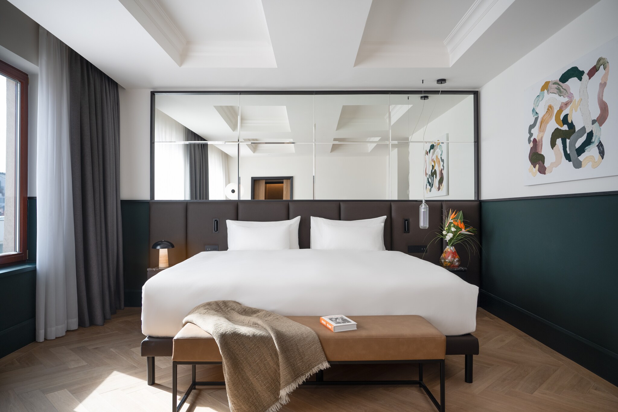 The bedroom of the Presidential Suite at Almanac X Alcron Prague is modern, with forest-green wainscoting, abstract art, and parquet floors.