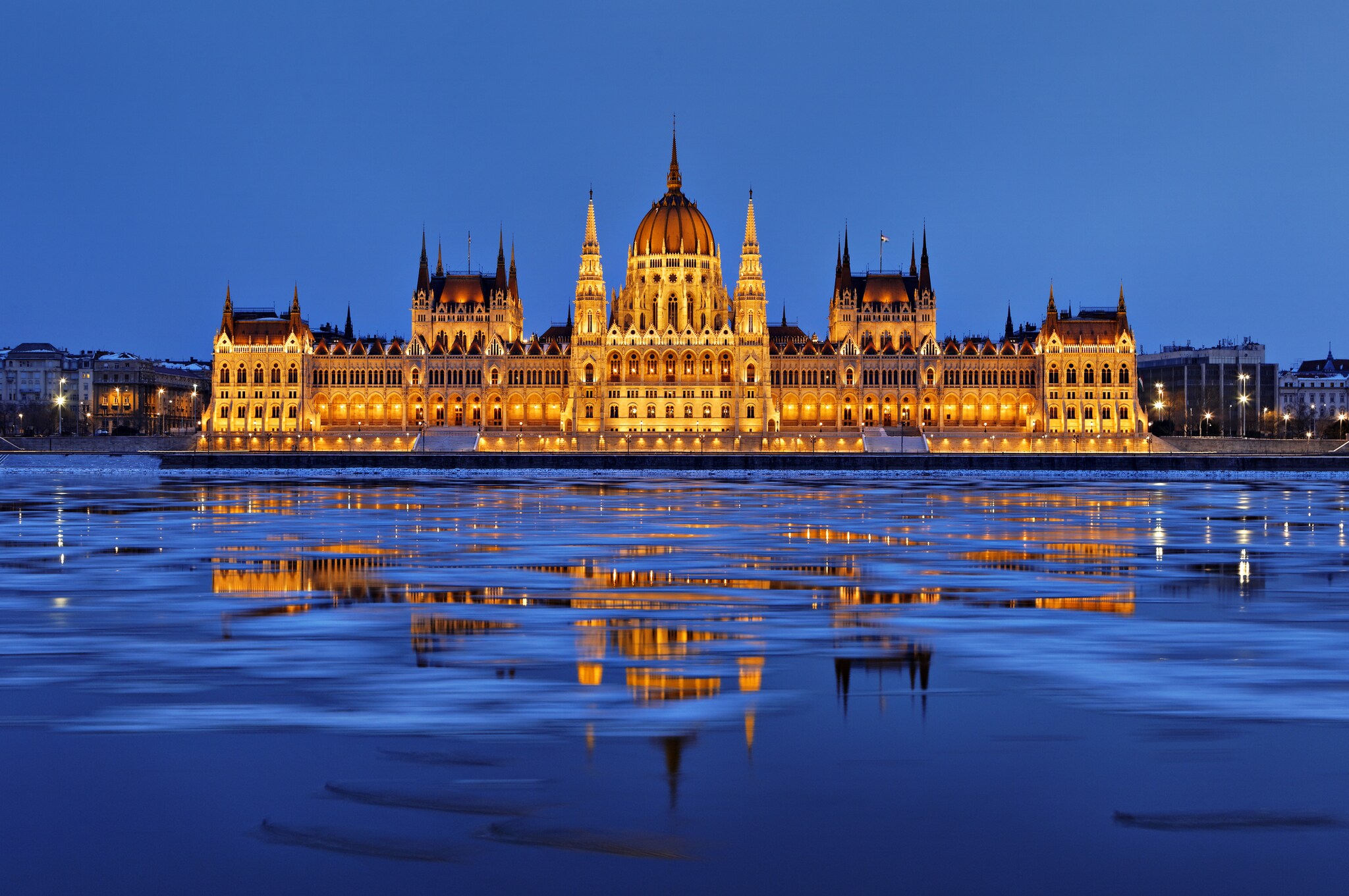 View from just above the waters of the Danube, calm patches of which reflect parts of the gothic revival Hungarian Parliament Building.