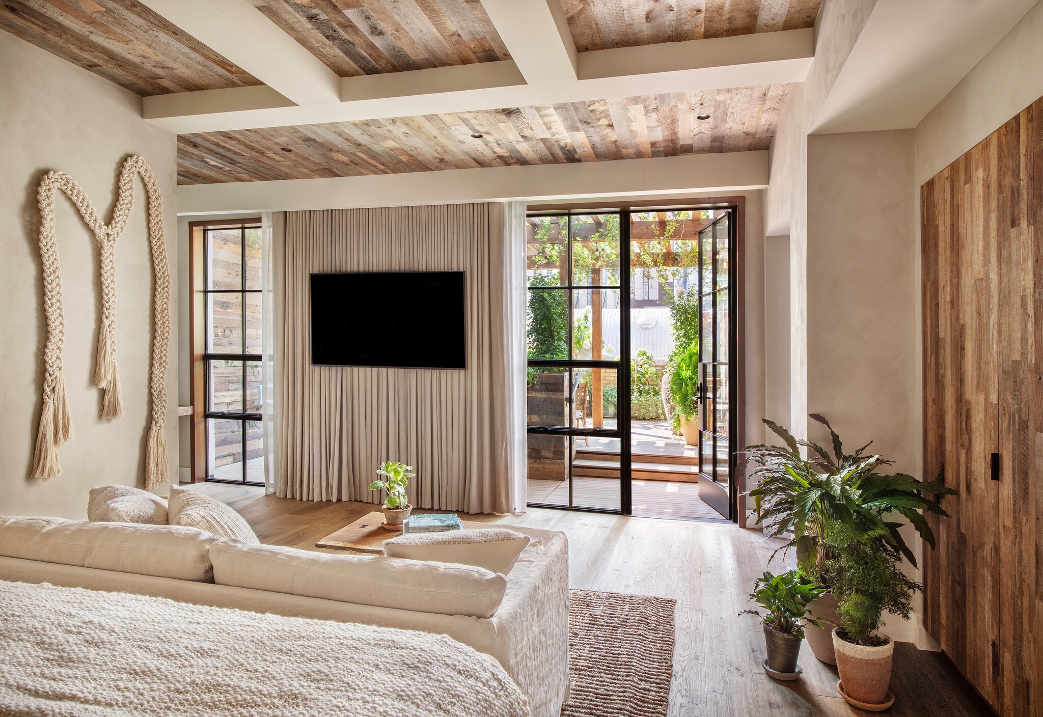 The Pergola King Terrace room has neutral tones and natural finishes, with a macrame wall hanging for flair. Glass doors open to a terrace.