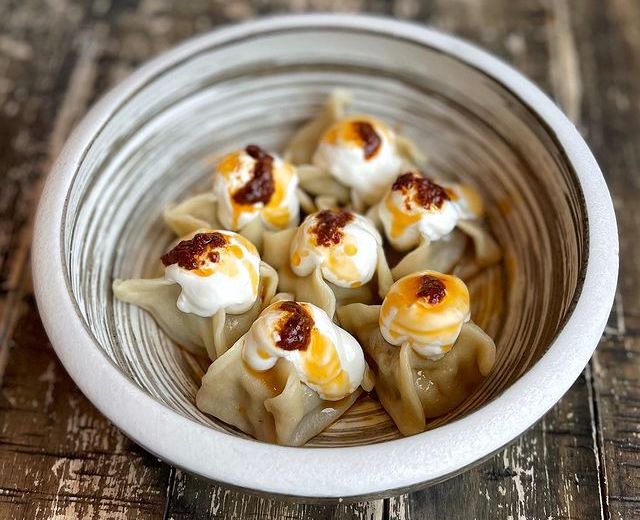 A bowl of ravioli topped with dollops of sour cream and a drizzle of red pepper butter.