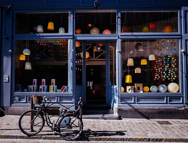 Street view of a lighting store with wide windows showing off lamps and fixtures. The building is blue and a bike is parked out front.