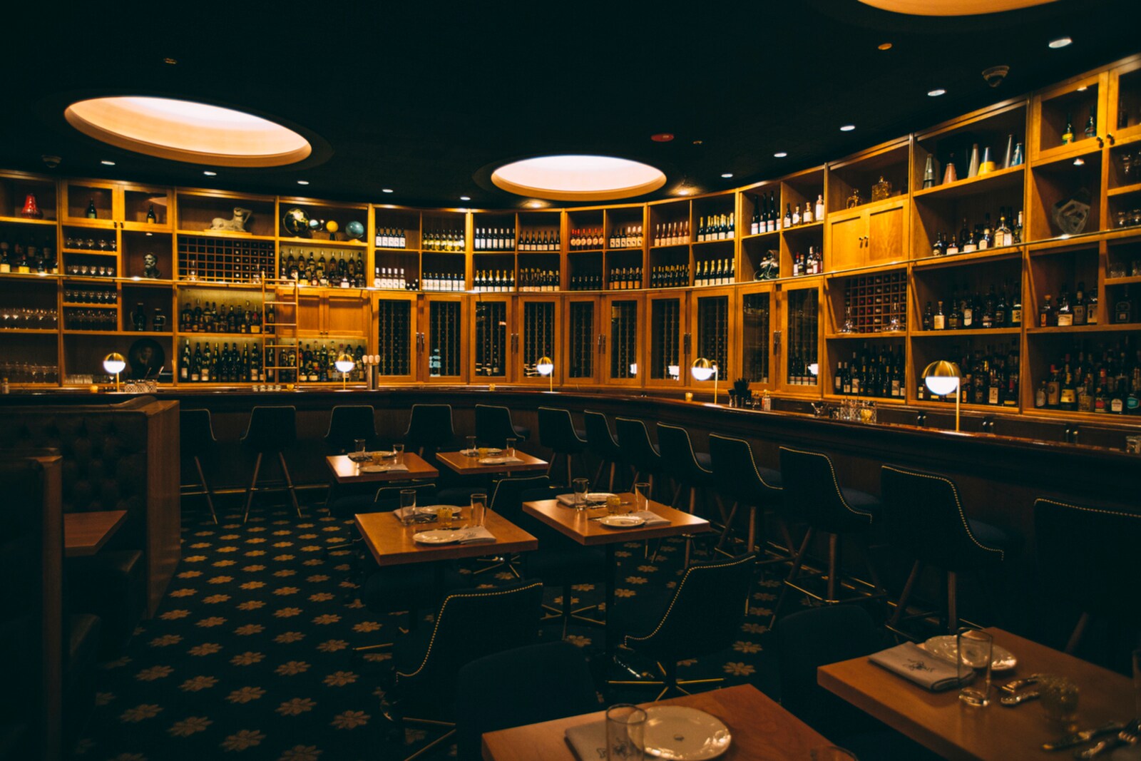 Cherry Circle Room is dark, with blue-black and gold décor tables and booths. Stools line a bar along the walls under shelves of bottles.