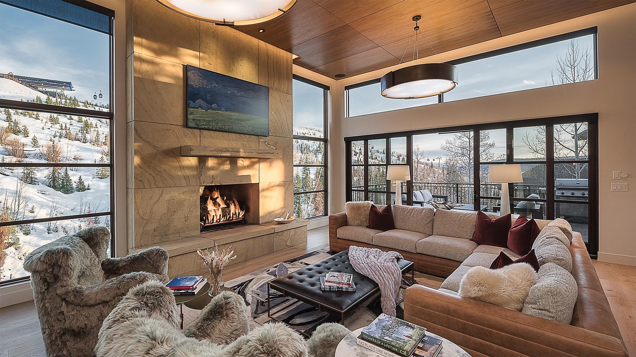 Modern living room with fireplace with view of snowy mountainside though expansive windows in winter.