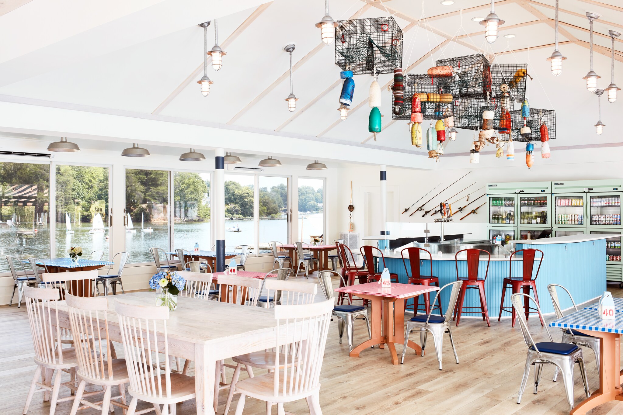 The interior of Fish Hawk Oyster Bar is bright, with windows and a white walls and ceiling. Buoys and lobster cages hang from the ceiling.