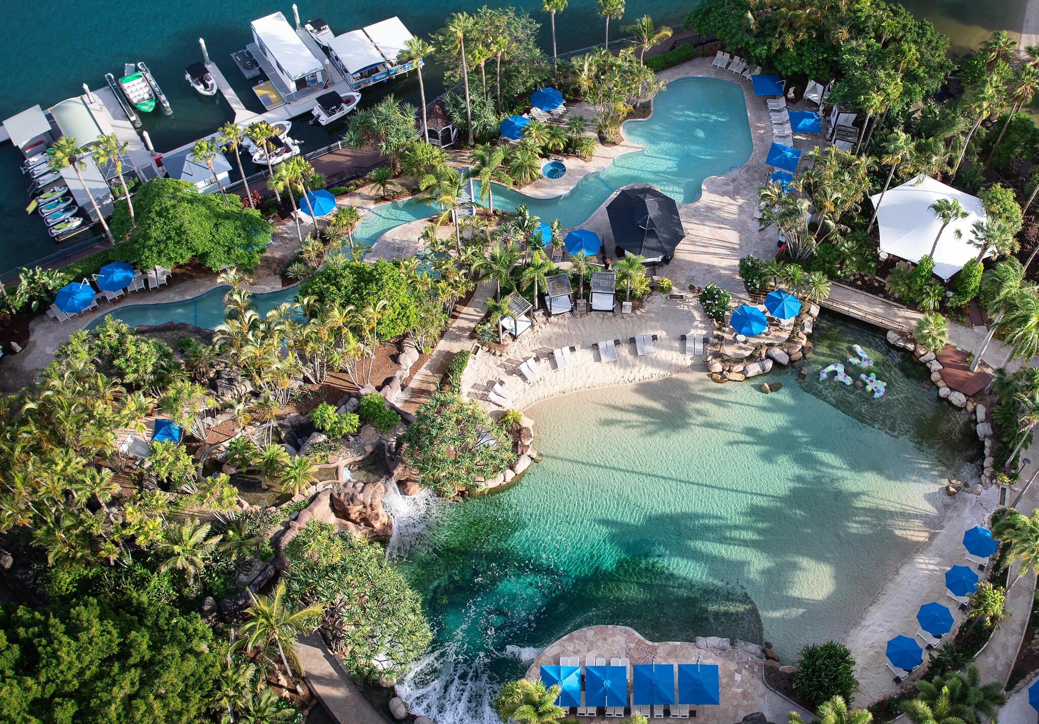 Aerial view of the lagoon and freshwater pool, which undulate between palm trees and rows of white lounge chairs and blue umbrellas.
