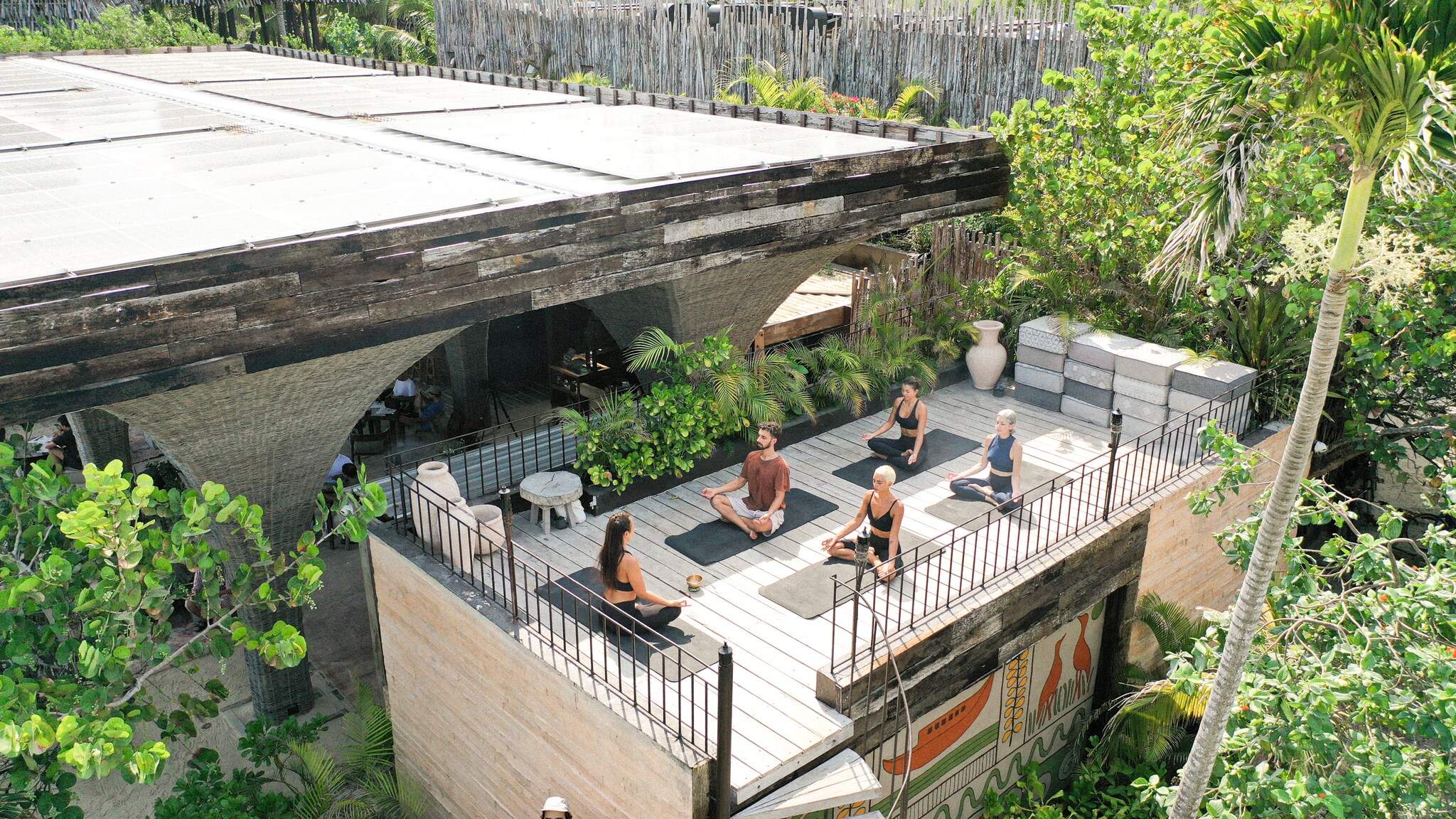 A multiracial, multigender group of vacationers in warm-weather workout gear sits cross-legged on yoga mats on a rooftop at Nomade Holbox.