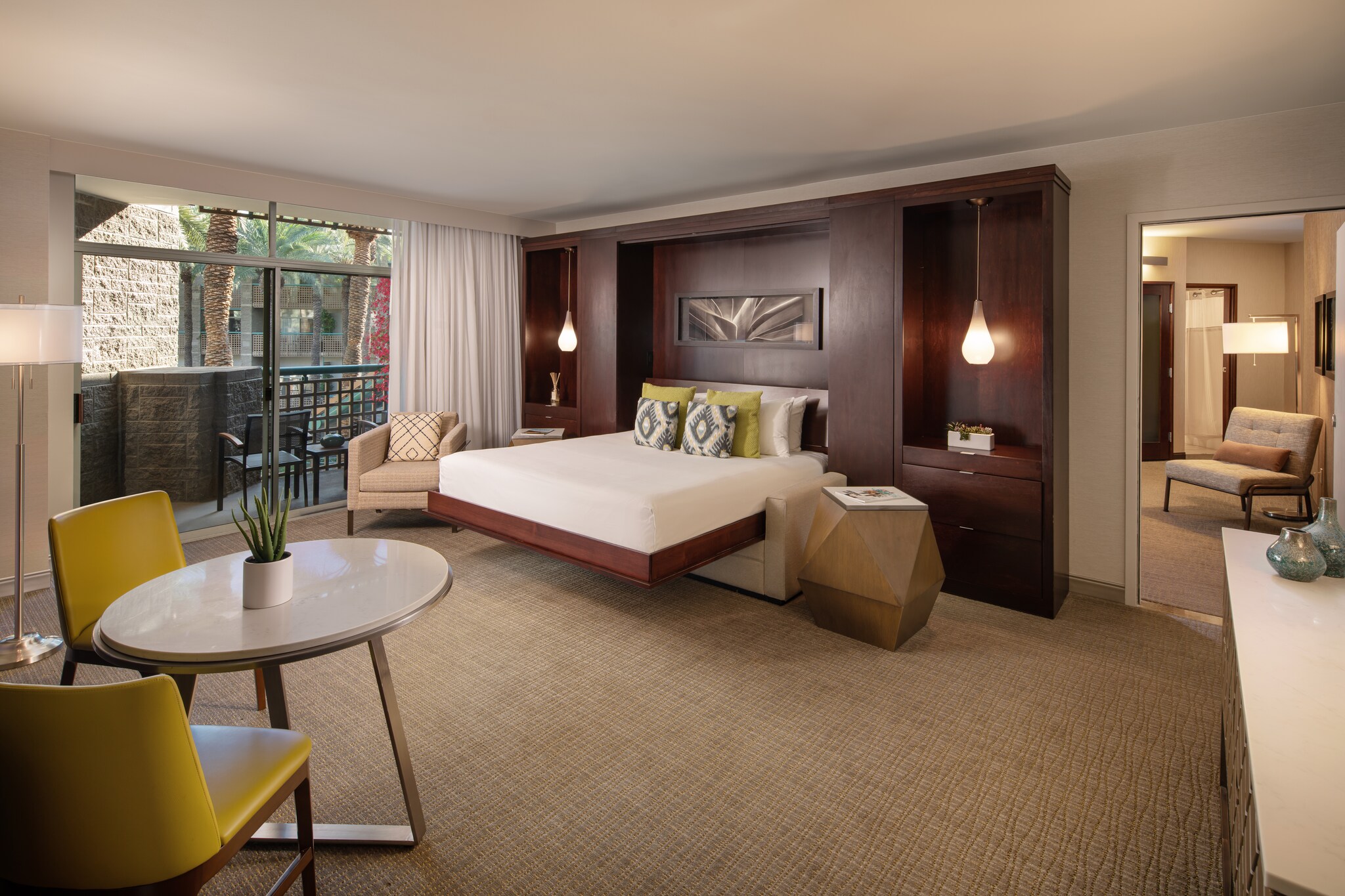 In a living area decorated in browns and greens, a sleek sofa bed extends from a dark wood set of shelves next to a geometric side table.