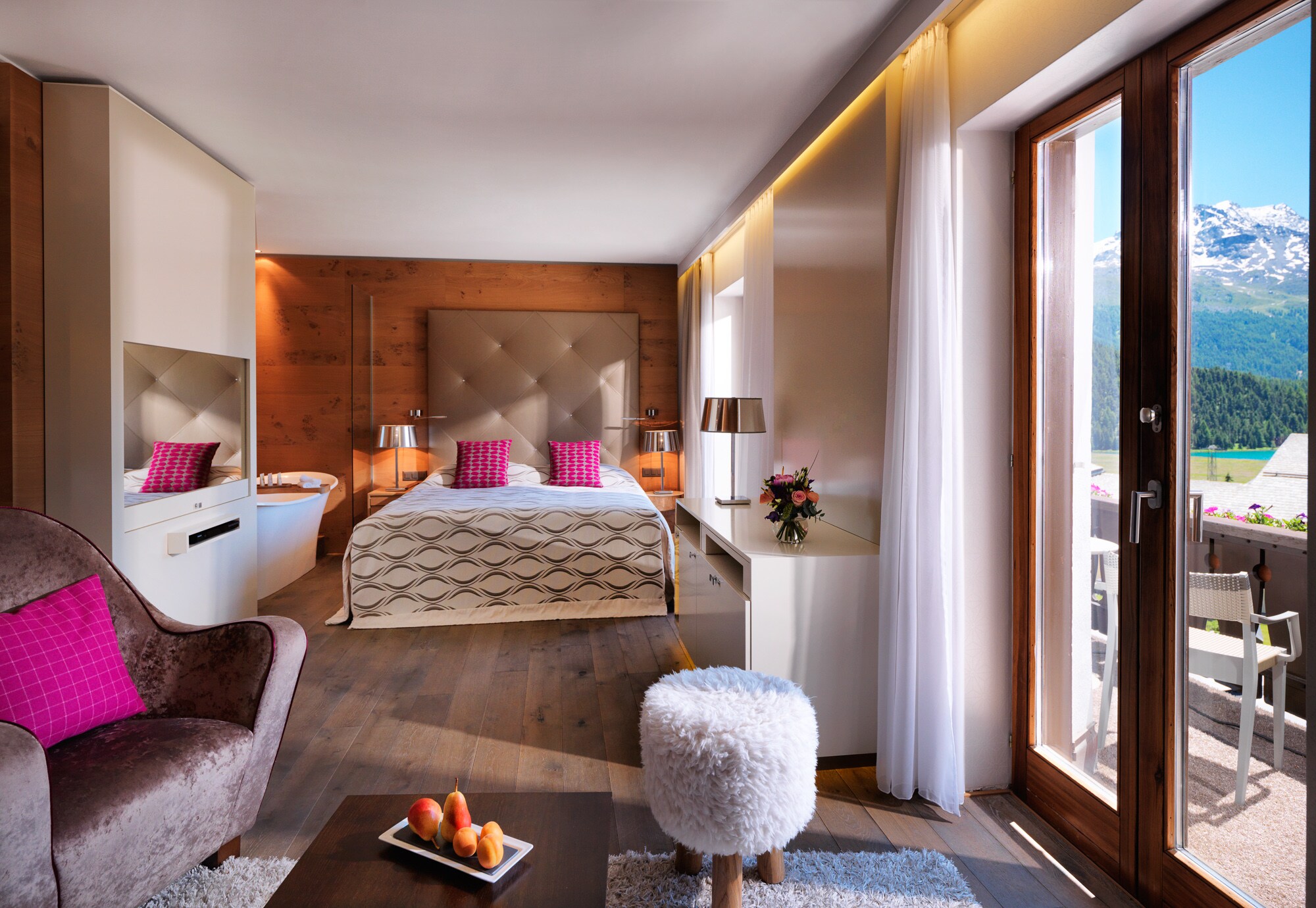 The bed in a Junior Suite has a high taupe headboard and magenta pillows. Nearby, a purple armchair is arranged to look out on a verandah.