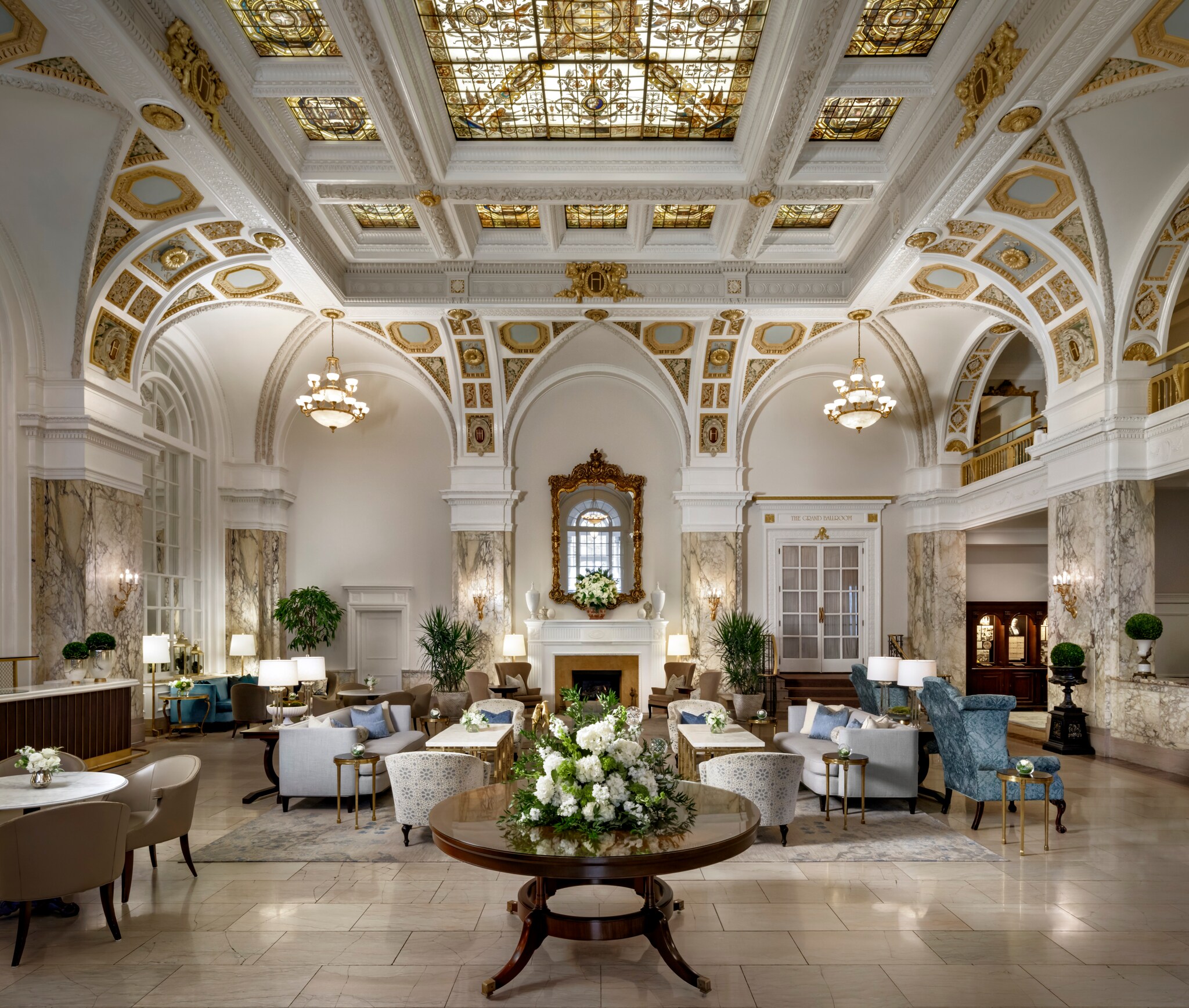 The Hermitage Hotel lobby has vaulted ceilings with stained-glass panels and gold molding. Below is white, blue, and brown seating.