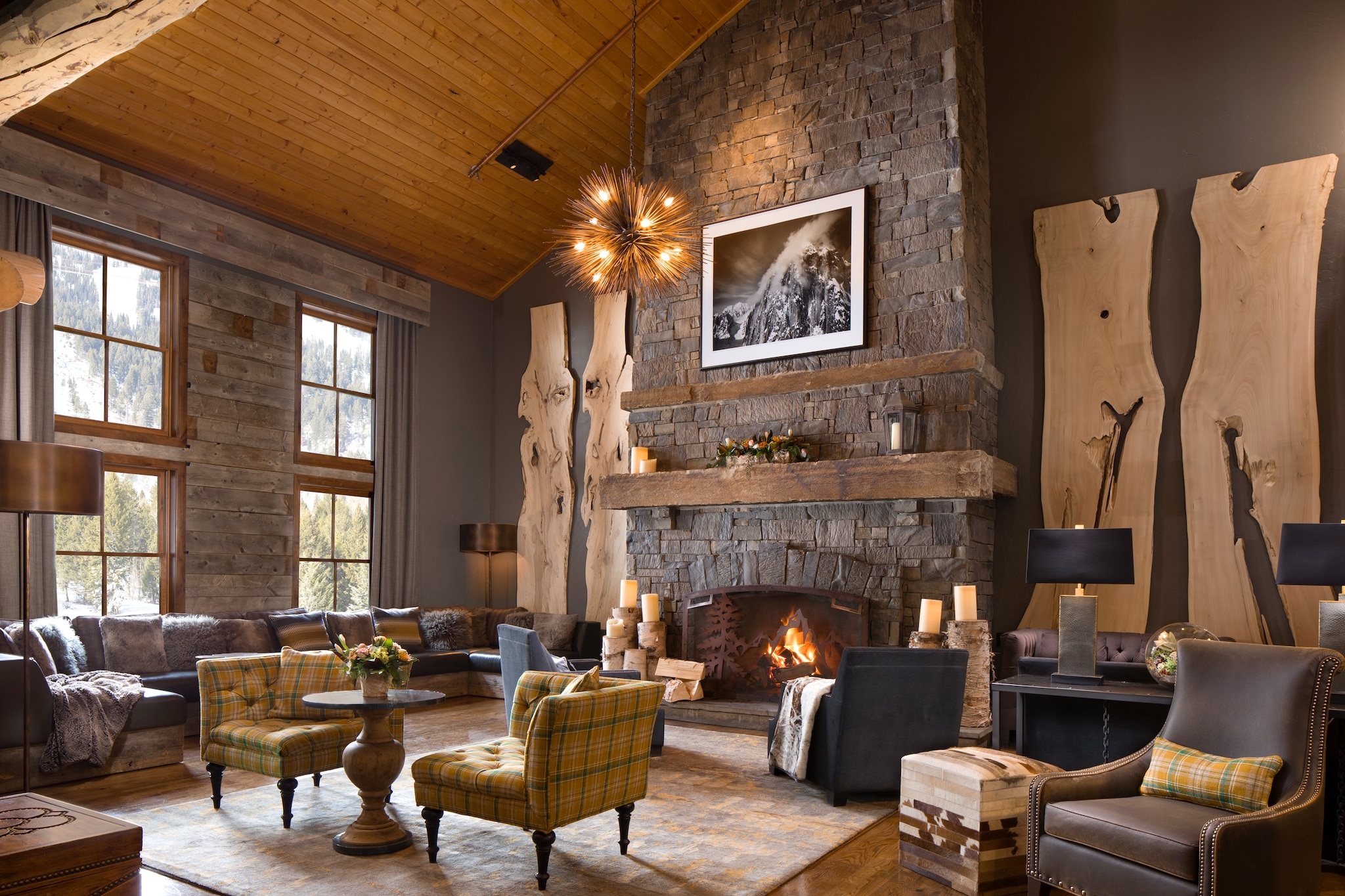 In a common area at Teton Village Lodge and Spa, leather couches and plaid chairs are arrayed around a stone fireplace.