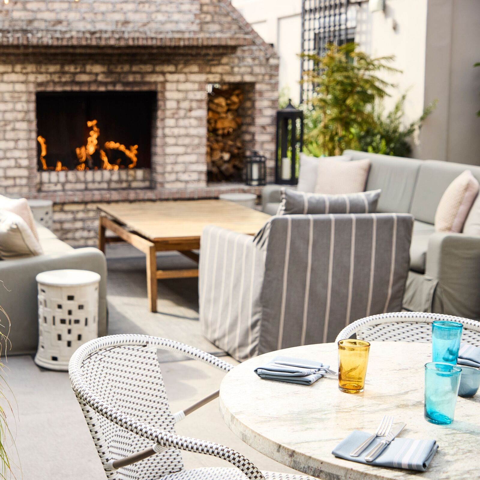 View over a white marble table set with colored glasses, towards gray couches and armchairs situated around a white brick fireplace.