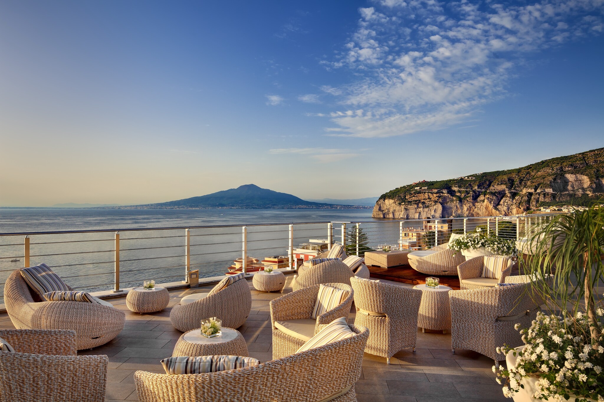 The Vista Sky Bar at Hotel Mediterraneo Sorrento is dotted with wicker chairs. Beyond the railing, the Gulf of Naples is tinged with sunset.