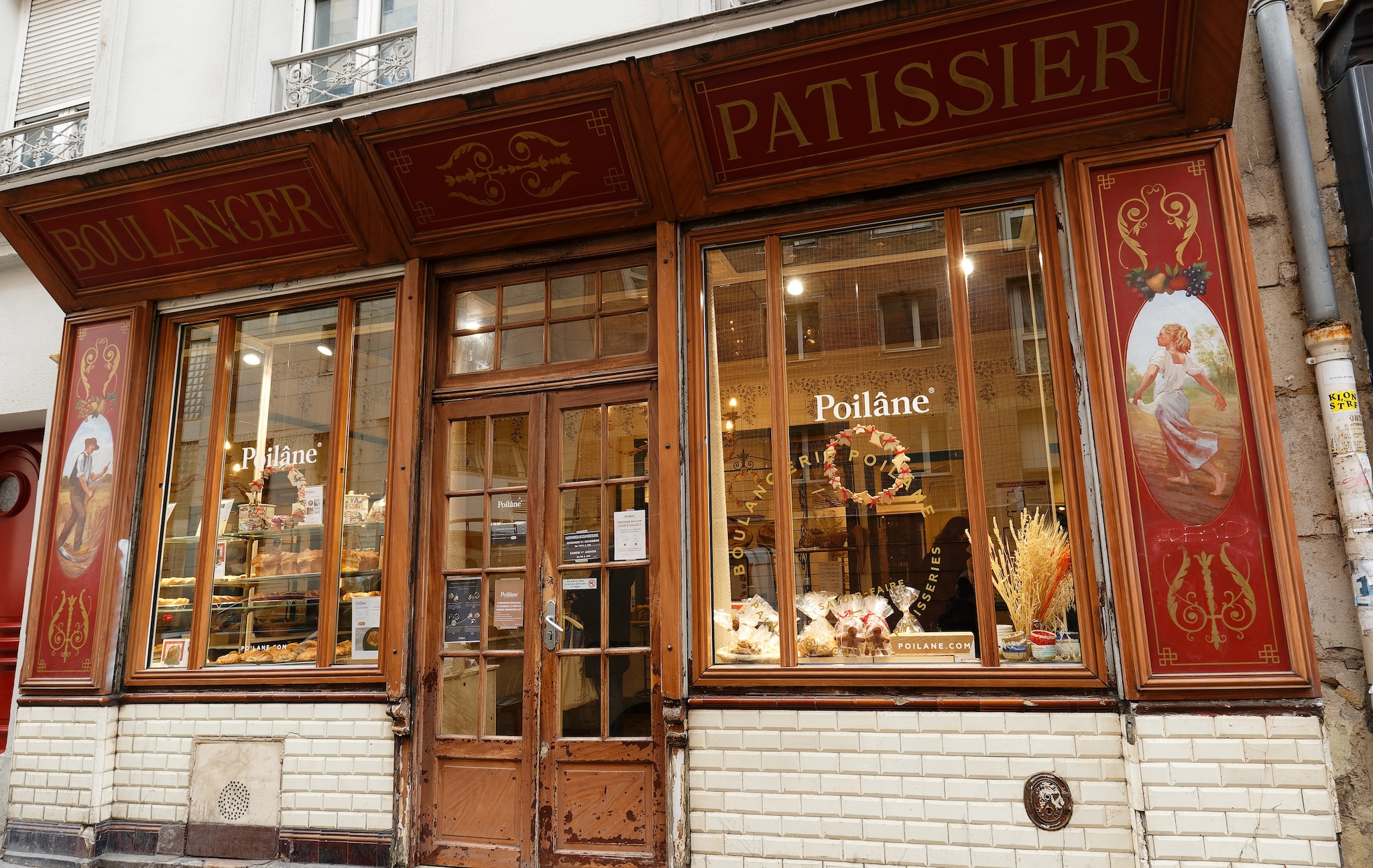 The storefront of Poilane bakery is white-bricked at the bottom, with red and gold painted panels around the doors and windows.