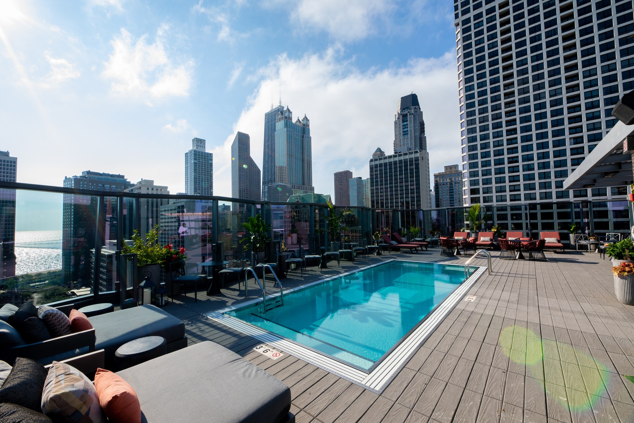 The 18th floor rooftop pool is rectangular, flanked by gray and orange sun beds. High glass railings provide views of the city.