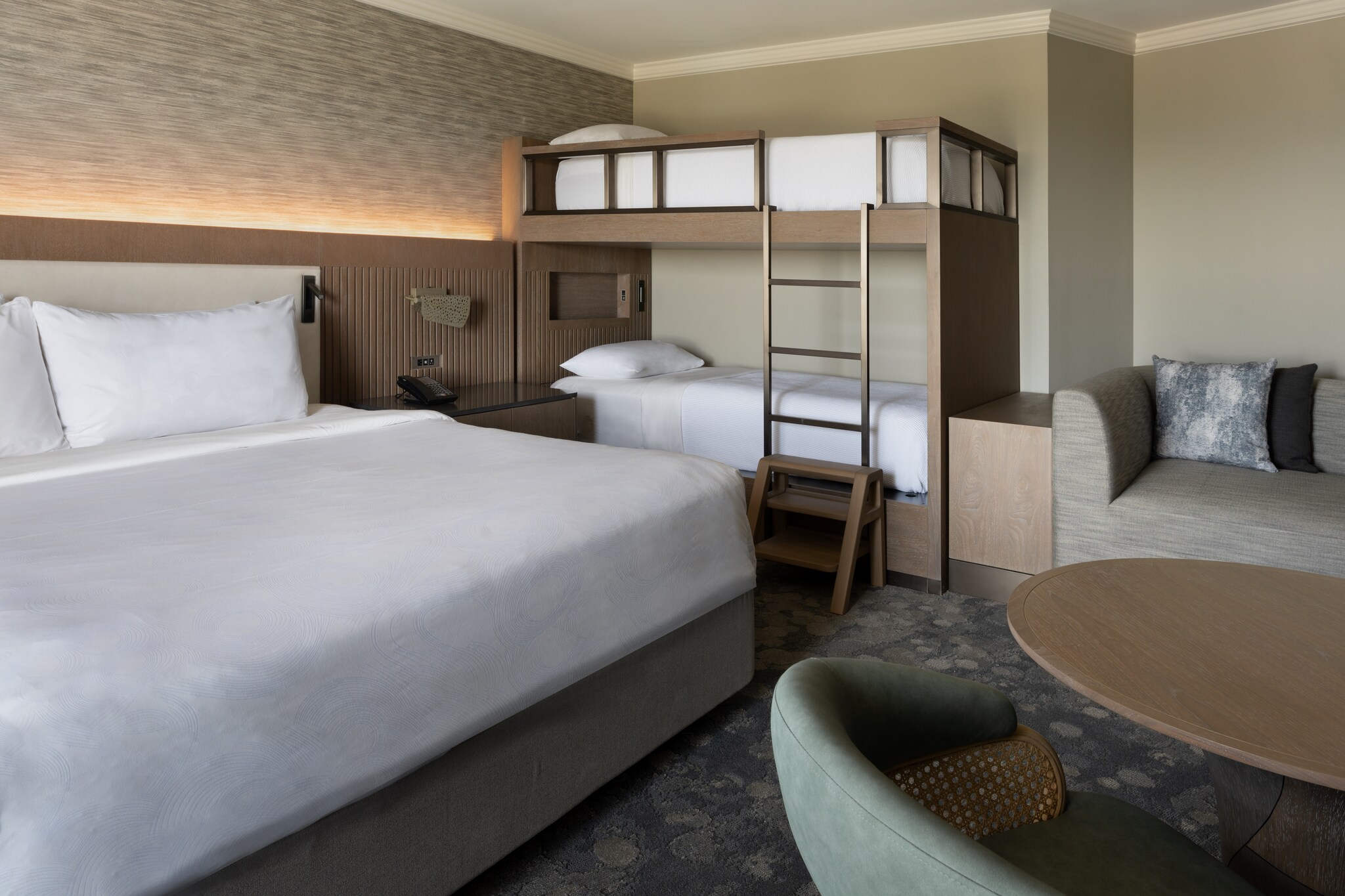 In a family suite decorated in soothing browns and grays, a large bed is separated from a bunk bed by a side table.