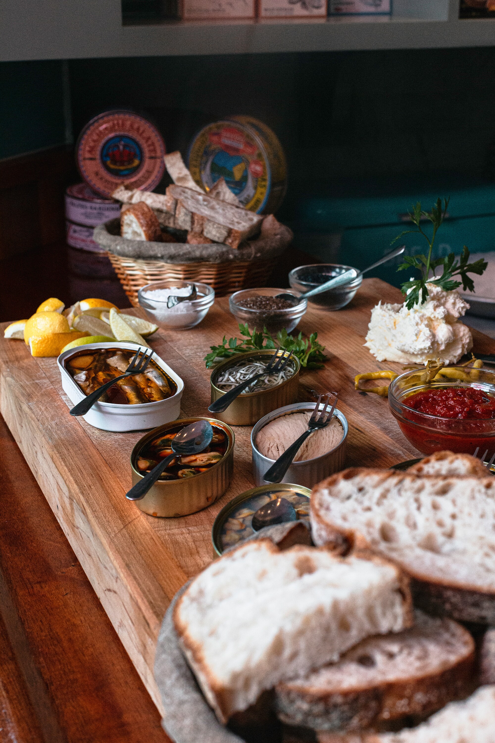 A charcuterie board is arrayed with lemons, herbs, dips, bread, and cans of tinned fish.