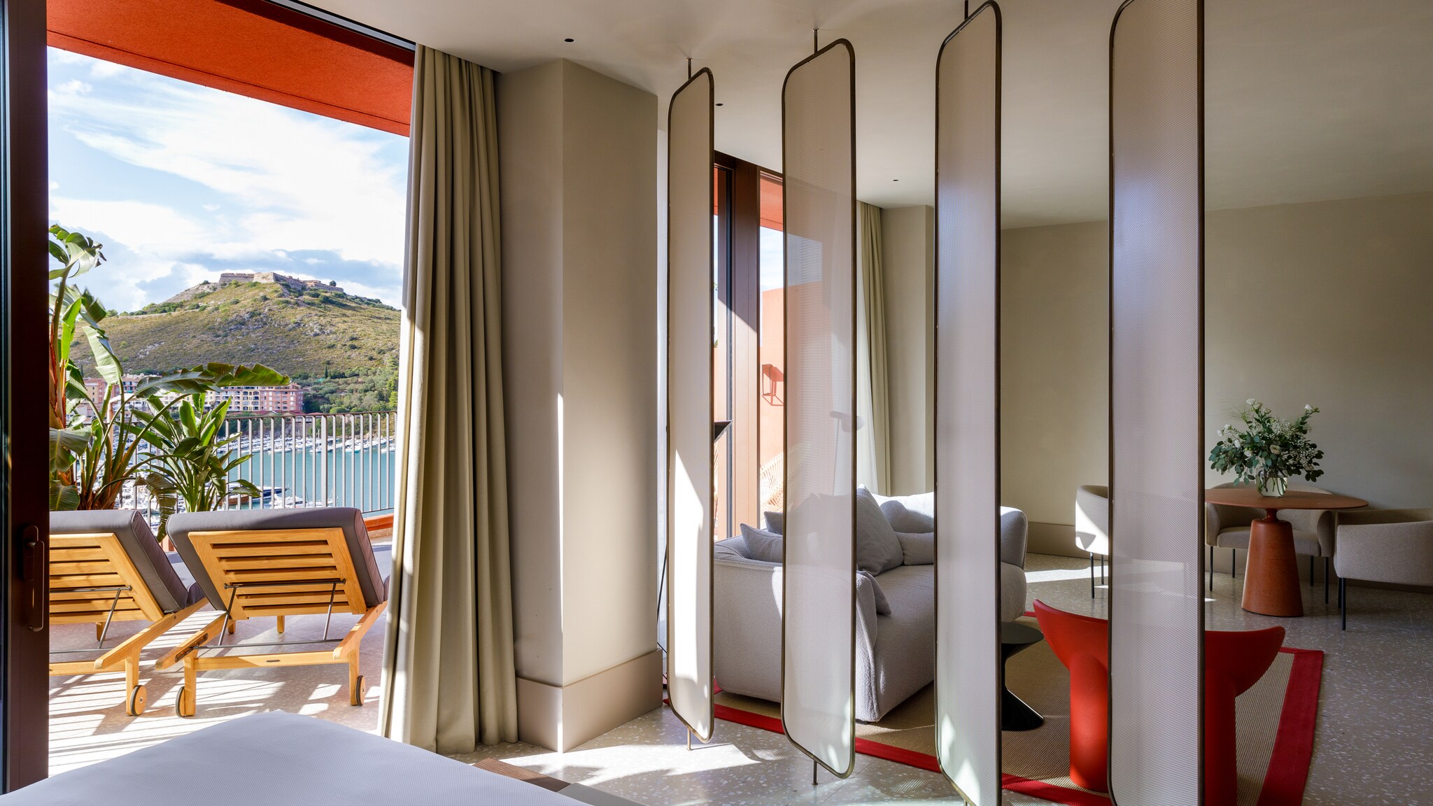 Past a line of small white screens in a La Roqqa guest room, a private terrace set with two navy-blue sun beds overlooks Porto Ercole.