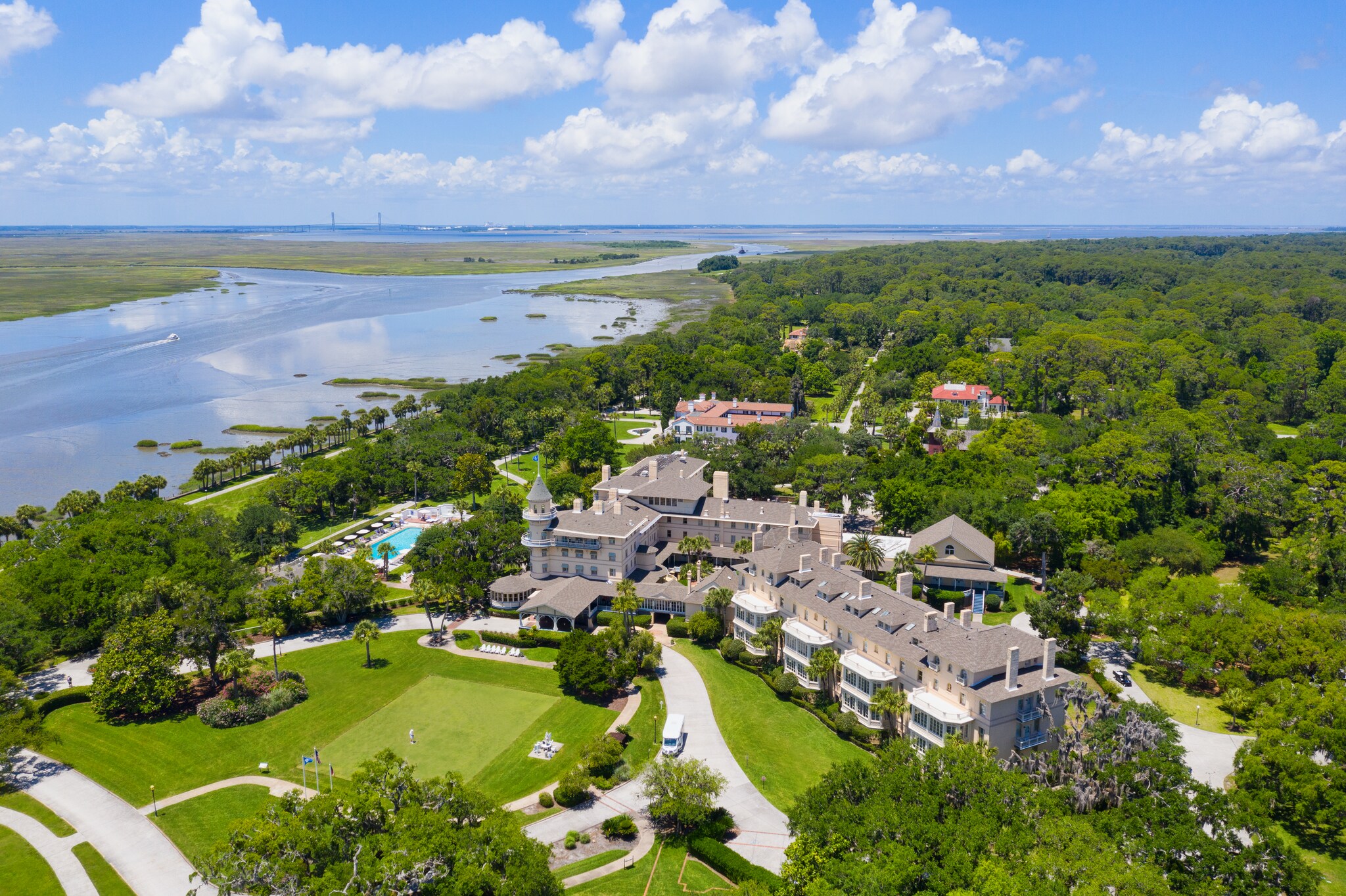 Aerial view of Jekyll Island Club, with long gray multistory buildings, lush forest, and the glassy surface of the Intercoastal Waterway.