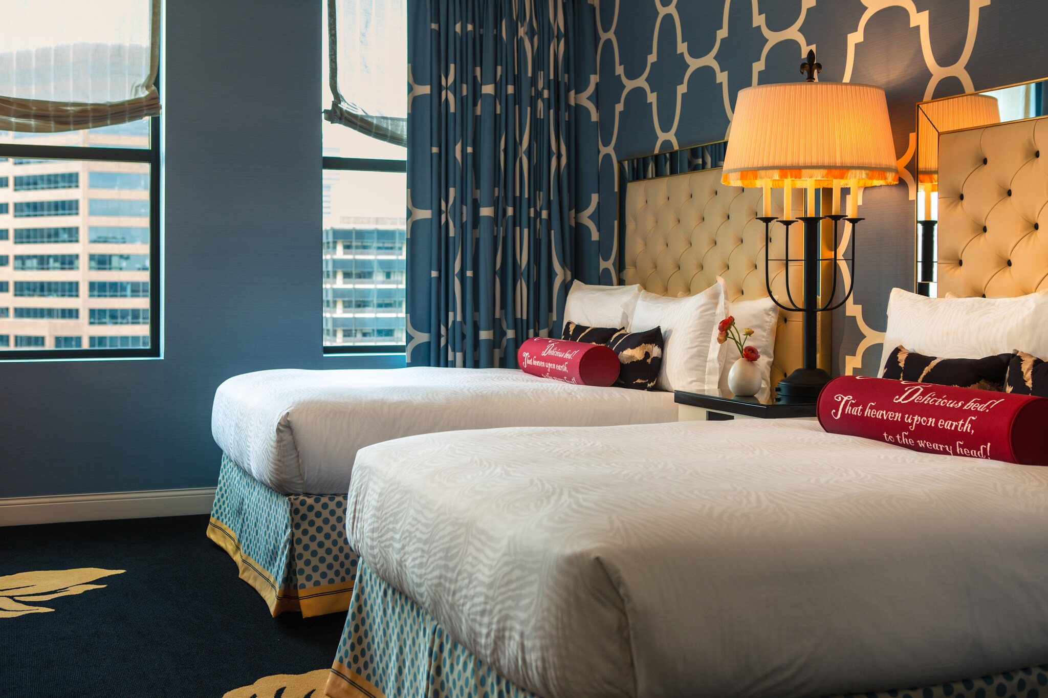 A double guestroom has blue carpets, walls, and wallpaper with gold accents, and the beds are set with pillows embroidered with poetry.